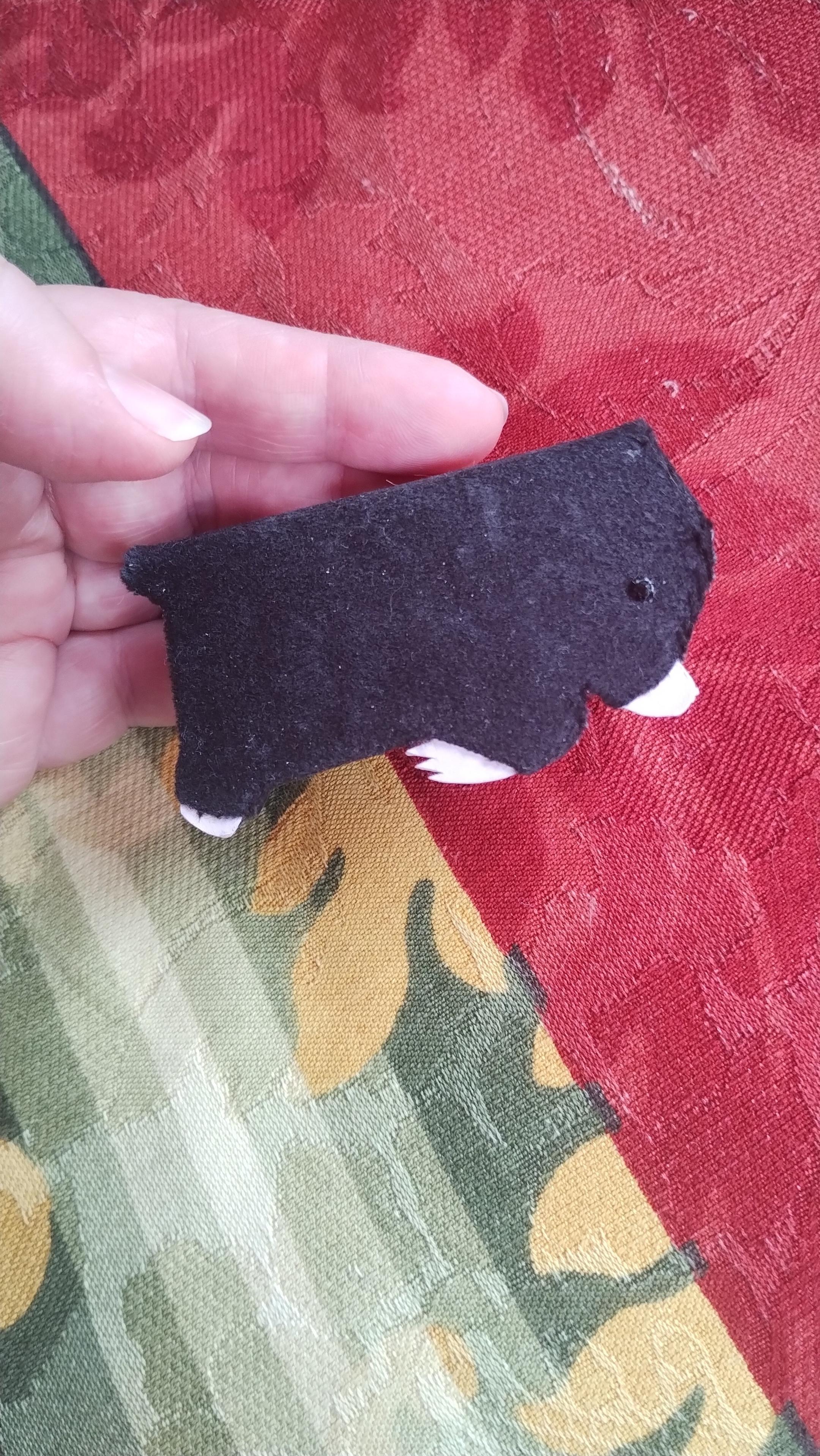 A small, approximately credit card sized book in the shape of a mole. It has short, velvety black bookcloth, pink little paws and nose, with a black resin dot for an eye.